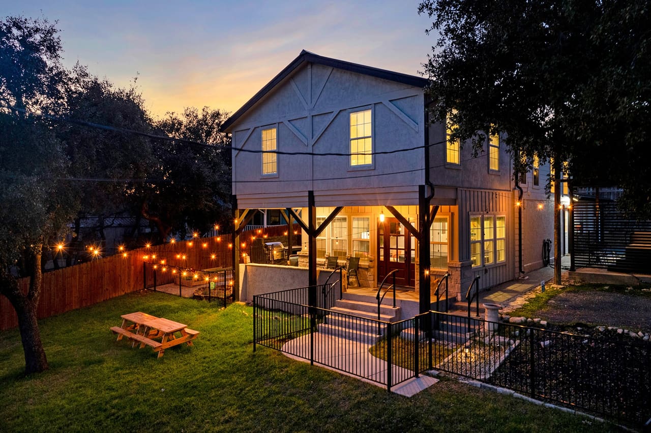 Cosmic Cowboy Retreat back of the two-story home at dusk with string lights, deck, and cornhole lawn