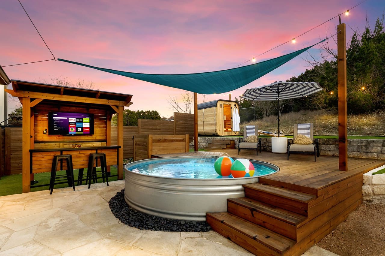 Cowboy Ridge stock-tank cold plunge under a shade sail with outdoor TV bar at sunset