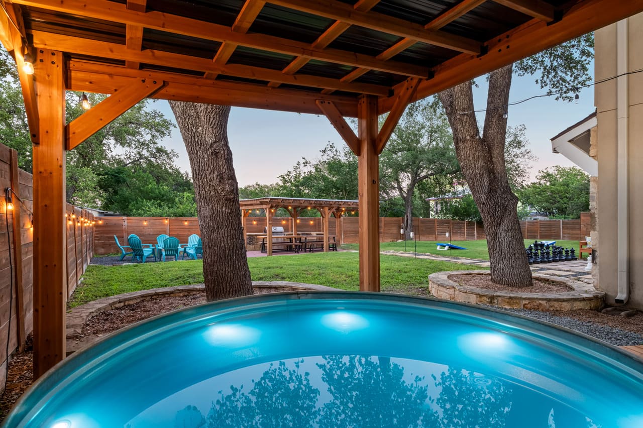 Dragonfly Escape stock-tank pool under a cedar pavilion with string lights and oak trees